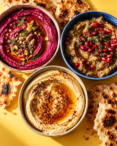 Three bowls of dips in tomato red, pistachio green and butter yellow with torn flatbread
