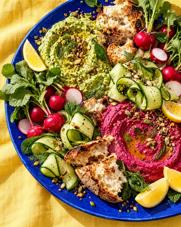A cobalt-blue board layered with colourful dips, torn bread and fresh vegetables
