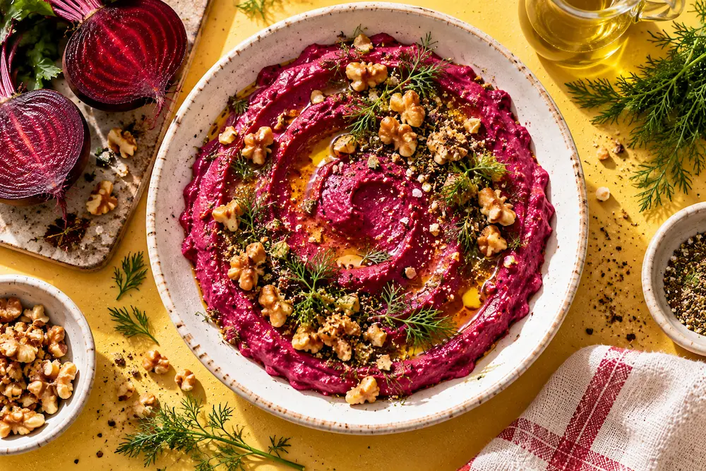 A vivid magenta beetroot labneh swirled in a bowl, topped with dill fronds, walnuts and olive oil