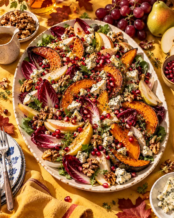 An autumn salad of roasted squash, pears, chicory and pomegranate arranged on a large cream platter